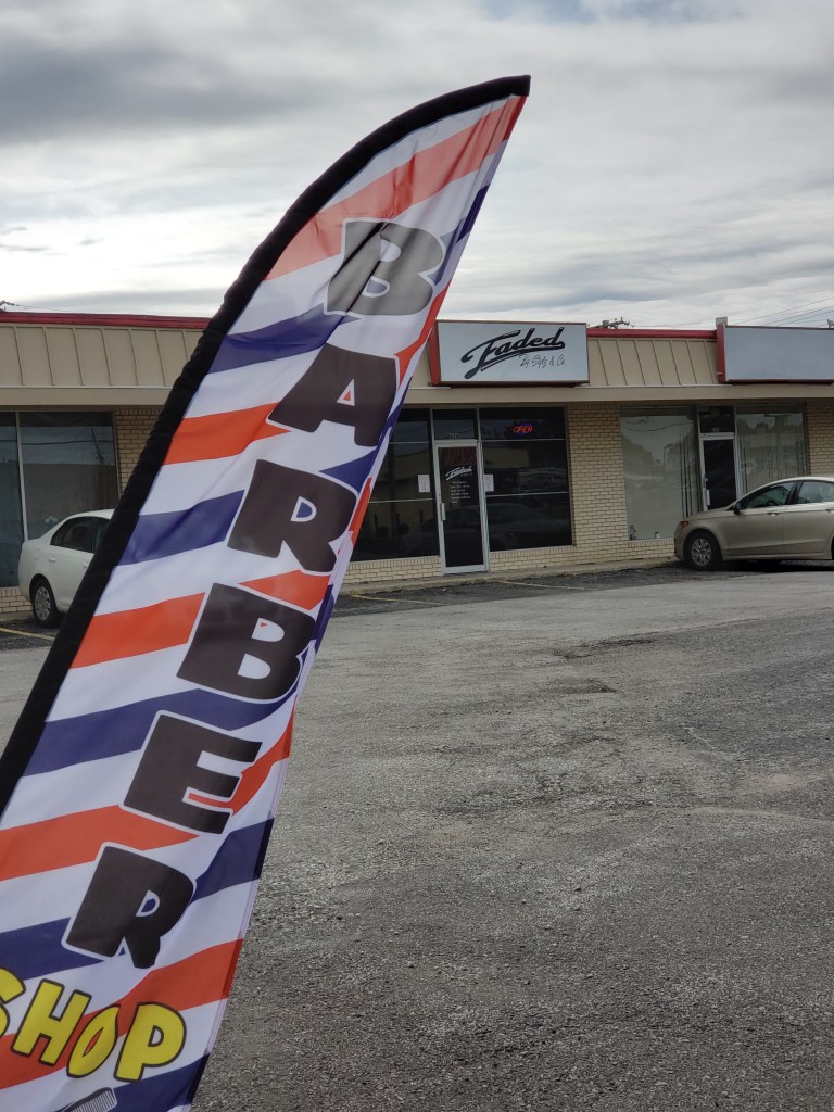 The barbershop banner in the foreground with the front of the shop in the background.