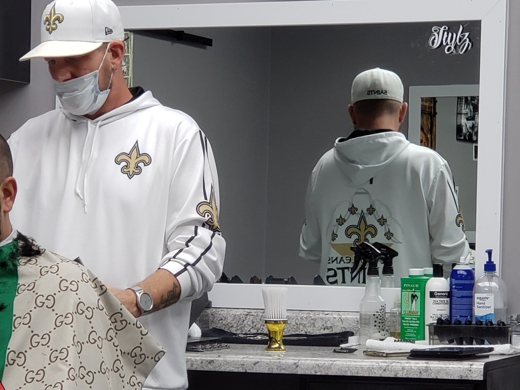 Stylz at his station with the back of his Saints hoodie reflected in the mirror.