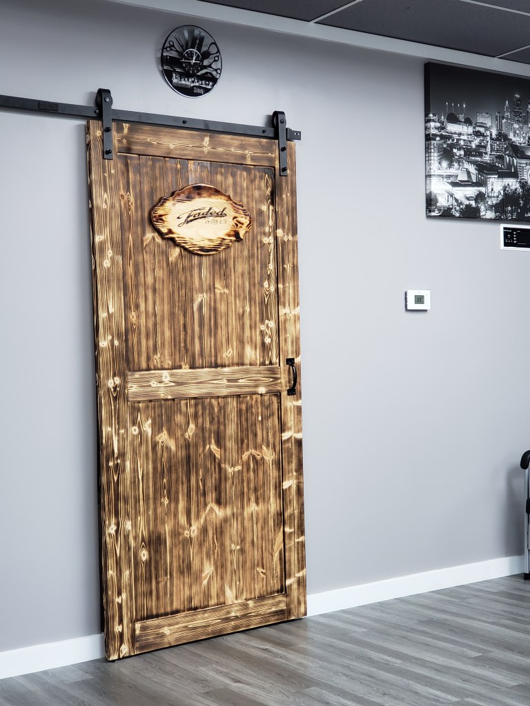 A barber shop themed clock cut from a vinyl record hanging over a wooden door with a woodburned Faded by Stylz & Co. sign on it.