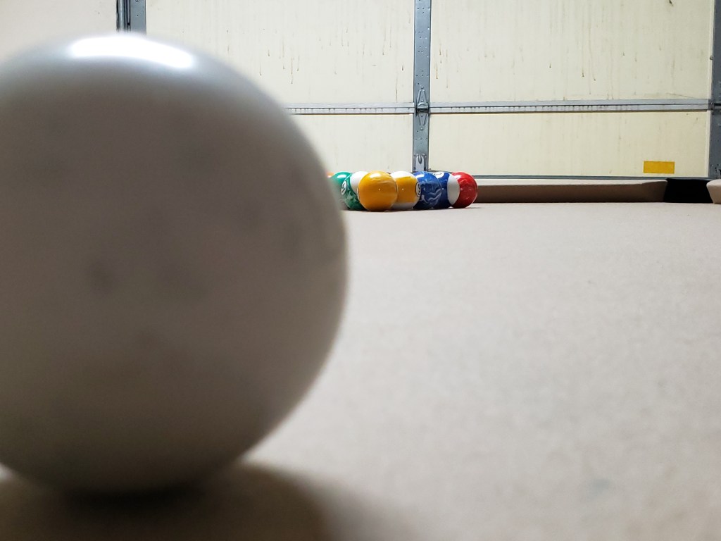 Looking across the pool table just past an out-of-focus cue ball in the foreground.