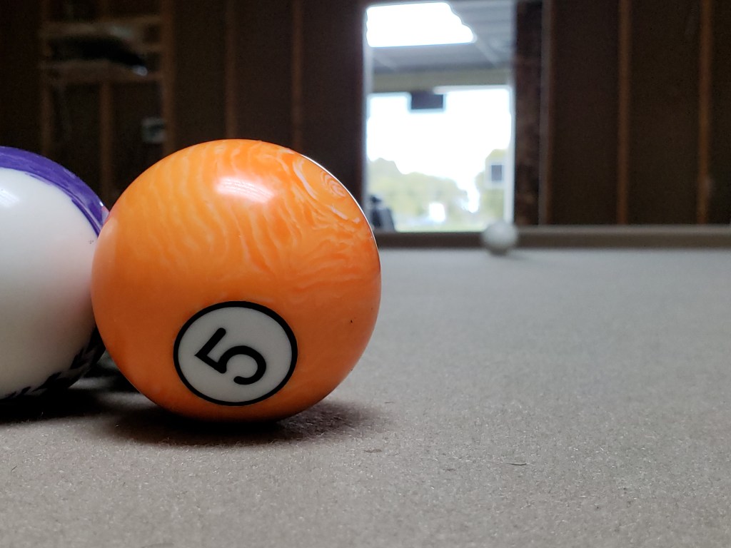 The 5 ball on the pool table with the shop out of focus in the background.